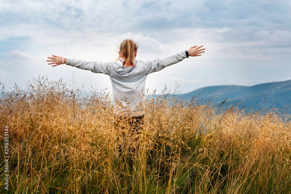 A young girl in the mountains is resting, looking at the sky and stretching her arms up. The girl feels free in the mountains like a bird, she thanks God for her life A young girl in the mountains is resting, looking at the sky and stretching her arms up. The girl feels free in the mountains like a bird, she thanks God for her life