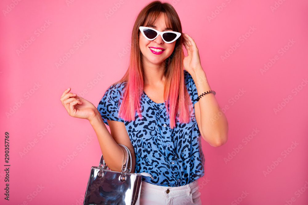 Naklejka premium Studio shot of woman in blue leopard t-shirt isolated on pink background.Portrait of a cheerful young girl in casual fashion look looking at camera and winking isolated over pink background.Copy space