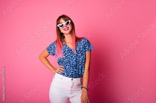 Studio shot of woman in blue leopard t-shirt isolated on pink background.Portrait of a cheerful young girl in casual fashion look looking at camera and winking isolated over pink background.Copy space © ClaudiK