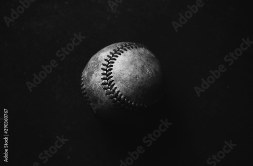 Low key baseball closeup in shadows with black background. Dark and moody sports image.