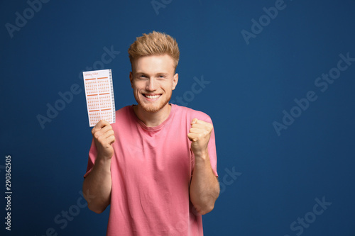 Portrait of happy young man with lottery ticket on blue background