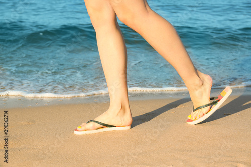 Closeup of woman with flip flops on sand near sea. Beach accessories