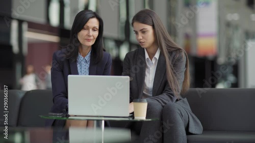 Wallpaper Mural Two businesswomen sitting at glass table on sofa discussing project on laptop computer. Experienced mature mentor giving advice to young colleague, tracking medium shot Torontodigital.ca