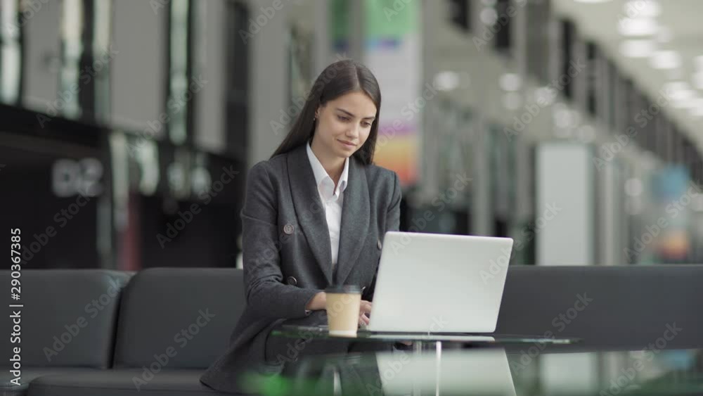 Young female entrepreneur working on laptop computer and thinking sitting on leather sofa at glass table in office lobby or airport lounge Young female entrepreneur working on laptop computer and thinking sitting on leather sofa at glass table in office lobby or airport lounge