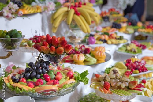 fruits are on the table .strawberry, black grape, apple, orange, banana, pomegranate, lemon tangerine, pear . chopped fruits over white table top