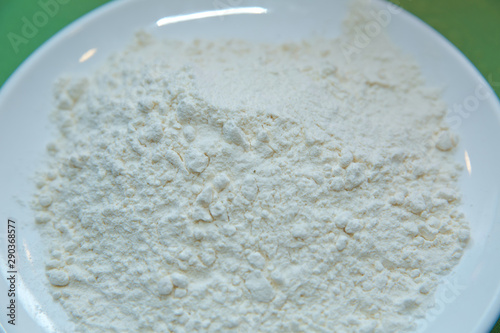 Flour in the plate green background . Close-up heap with wheat flour coarse in white plate on green background. Left on the photo . Portion of Milk Powder close-up shot on green background