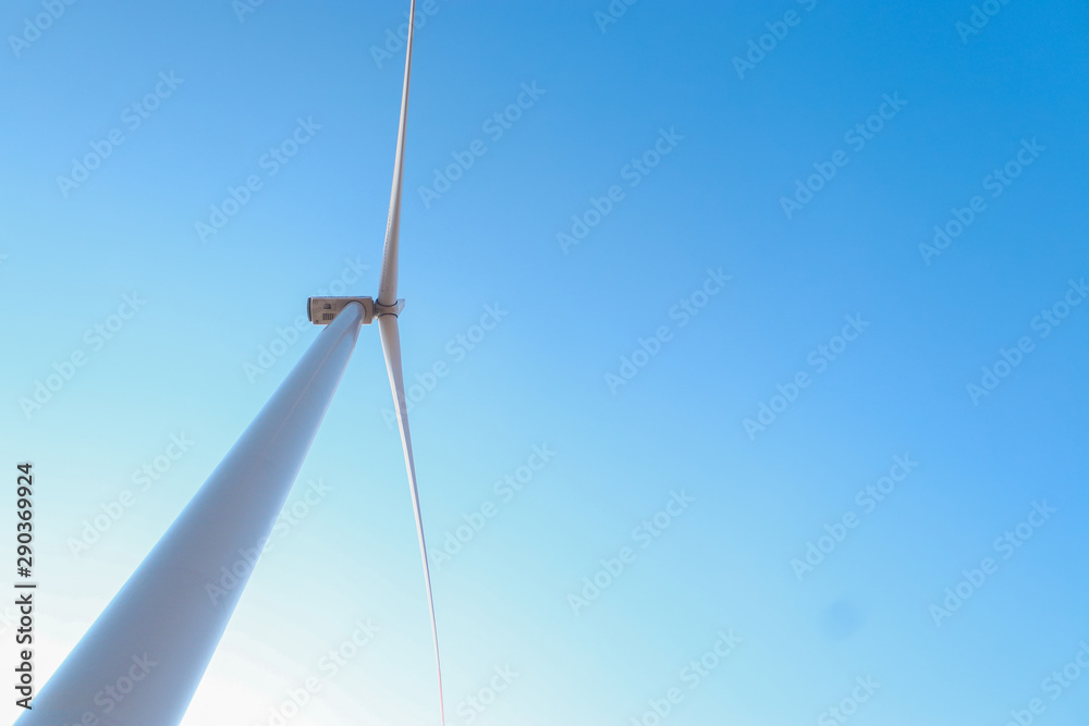 Looking upward to a big wind turbine and a blue sky. Alternative energy source, production and power generation. Ecology and freedom concept