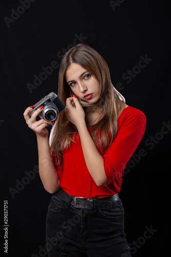 Beautiful girl with oldstyle camera posing in red shirt on black background.