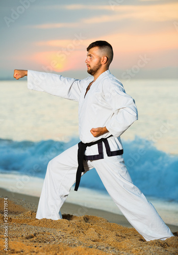 Man in uniform doing taekwondo exercises at sunset sea shore