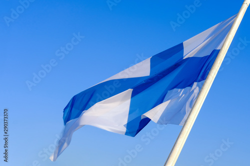 National flag of Finland waving on the wind against clear blue sky. Finnish flag on flagpole,