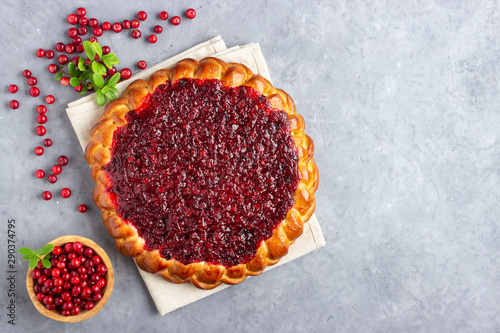 Homemade flavored pie with fresh cowberry or lingonberry on a gray stone background with branches of northern wild cowberry.