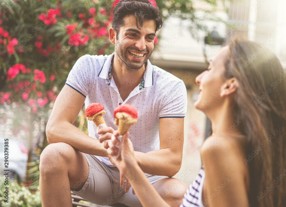 Young couple of lovers chatting and having fun eating an ice cream outdoors