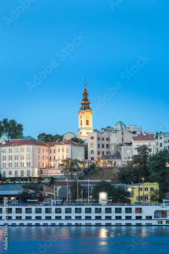 Blue hour view of Belgrade riverfront with Sava river in the foreground, holy archangel Michael cathedral at the back and impressive, large cruiser ship in the harbor