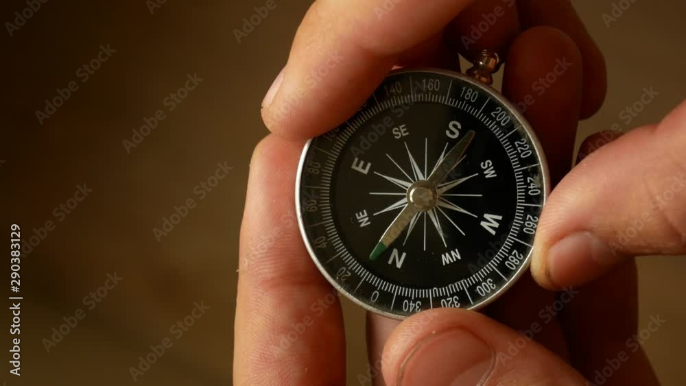 Male hands hold the compass and set needle to the north. Checking direction with a compass in hands. Close up shot of a spinning vintage compass. Male hands hold the compass and set needle to the north. Checking direction with a compass in hands. Close up shot of a spinning vintage compass.