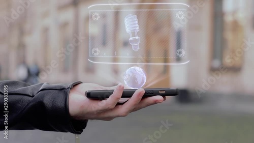 Male hands show on smartphone conceptual HUD hologram gas discharge bulb. Man with the future technology mobile holographic screen on blurred background of the university photo