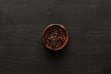 top view of brown bowl with whole peppercorns on dark wooden surface with copy space