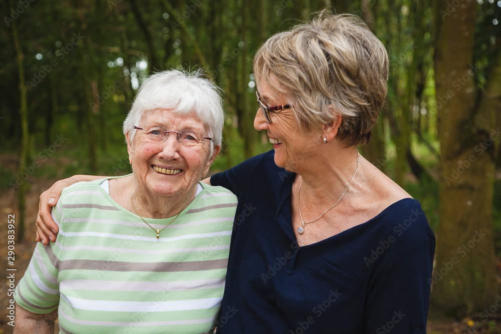 Senior lady with her aged mother with dementia, embracing and smiling in a summer park Senior lady with her aged mother with dementia, embracing and smiling in a summer park