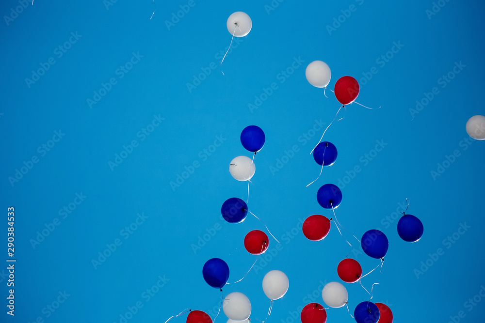 Red, white, blue helium balloons are flying into the blue sky