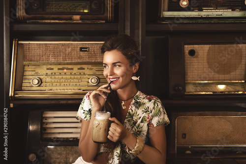 Young happy woman drinking iced coffee in stylish retro cafe photo