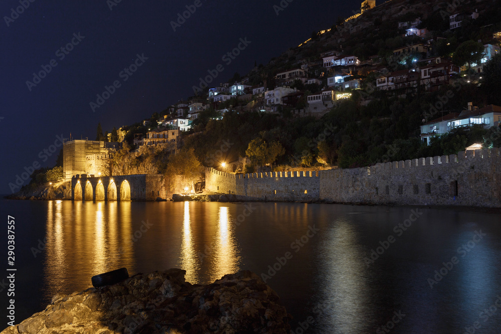 Shipyard with glowing lights close up. Night view of ancient shipyard with reflected light in the sea. Alanya, Turkey.