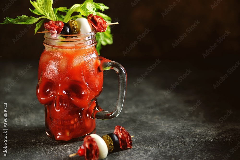 Bloody Mary cocktail in glass skull with celery sticks, pink salt, lime