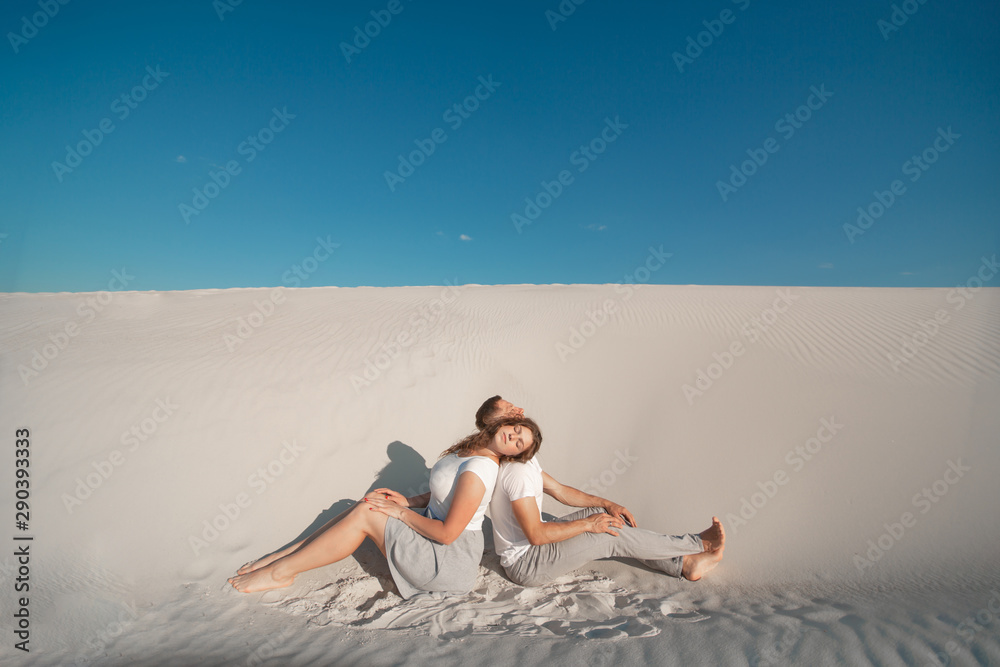 Romantic pair sit on white sand and huggins, in desert.