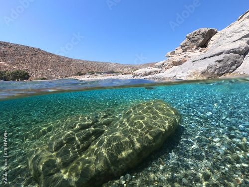 Above and below underwater photo of crystal clear turquoise pebble beach of Kaminakia, Astypalaia island, Dodecanese, Greece photo