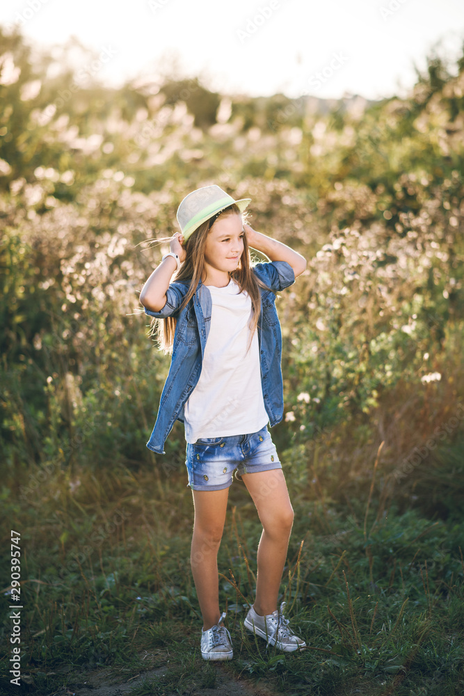 pretty little girl in shirt shorts and hat on sunset background