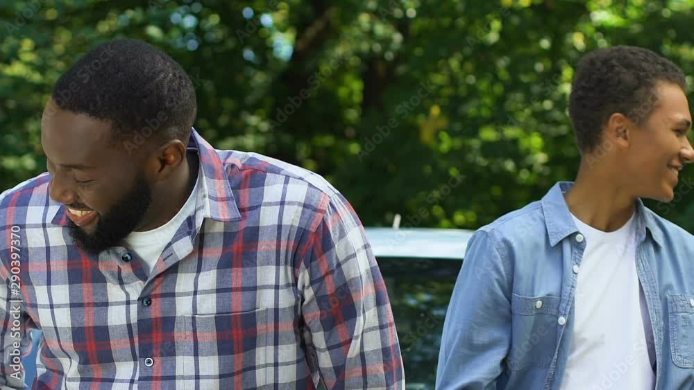 Smiling black dad throwing car keys to teenage son, both getting in vehicle Smiling black dad throwing car keys to teenage son, both getting in vehicle