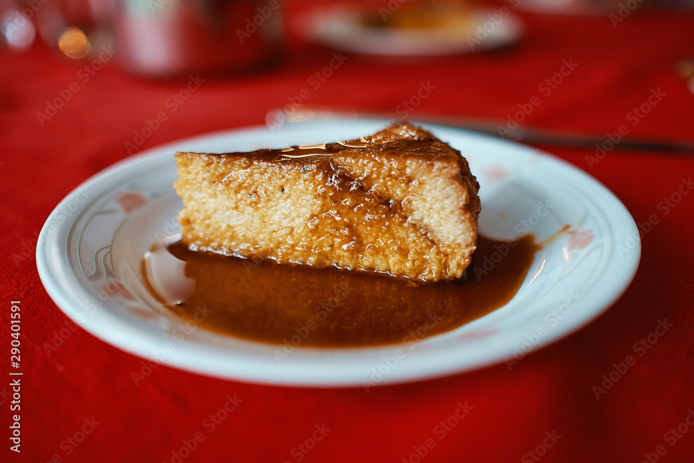 piece of flan served in a white plate on a red tablecloth, you can see the layers and melted caramel piece of flan served in a white plate on a red tablecloth, you can see the layers and melted caramel