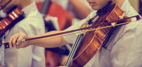 Asian boy students playing violin with music notation in the group. Violin player. Violinist hands playing violin orchestra musical instrument closeup. Symphony orchestra on stage. Selective focus.