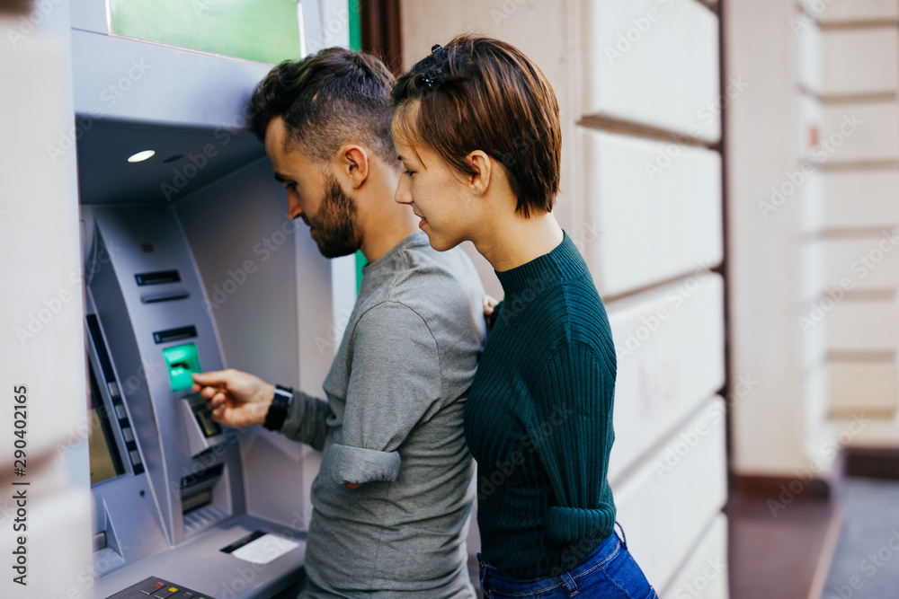 Disabled couple usinig ATM machine in city street. - obrazy, fototapety, plakaty 