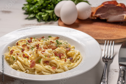Carbonara pasta with pancetta, egg, hard parmesan cheese and cream sauce. White plate on white wooden background. Traditional italian cuisine. Pasta alla carbonara