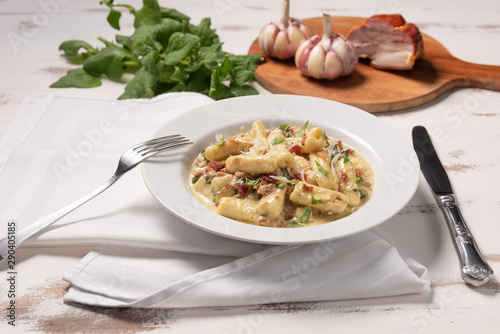 Penne pasta with carbonara sauce in white plate on wooden white background, soft light, angle view. Italian food