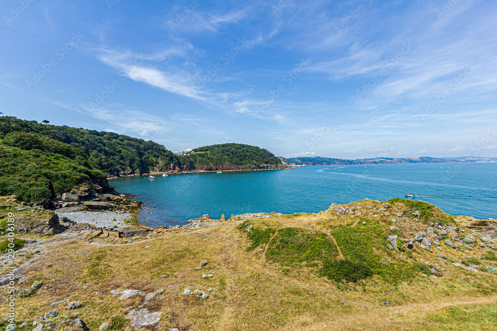 A panorama view of a beautiful bay with calm blue water surrounded by forest under a majestic blue sky and some white clouds