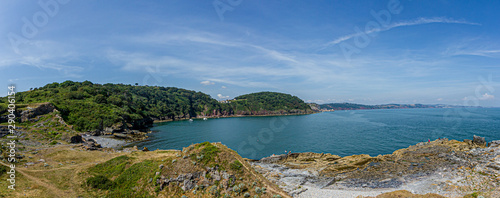 A panorama view of a beautiful bay with calm blue water surrounded by forest under a majestic blue sky and some white clouds