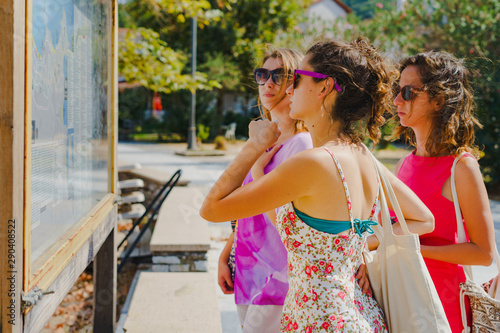 Three female tourist women looking at the map location on the info panel in the Greece tourist destination in a summer day on the vacation holiday information orientation