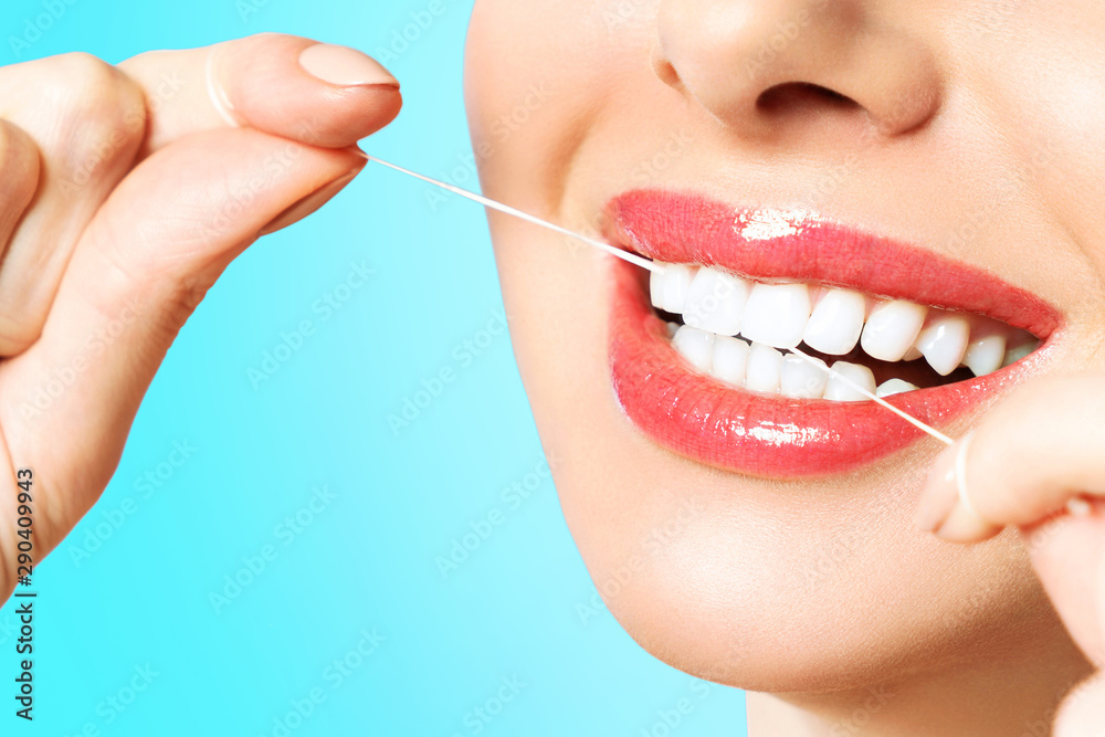 Obraz premium Young beautiful woman is engaged in cleaning teeth. Beautiful smile healthy white teeth. A girl holds a dental floss. The concept of oral hygiene.