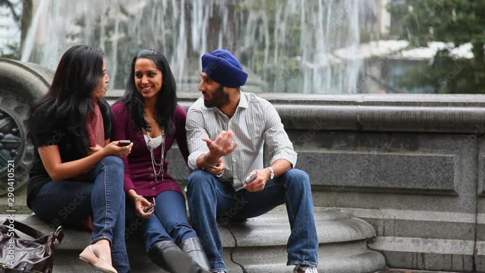 Friends sitting and talking at fountain in park Friends sitting and talking at fountain in park