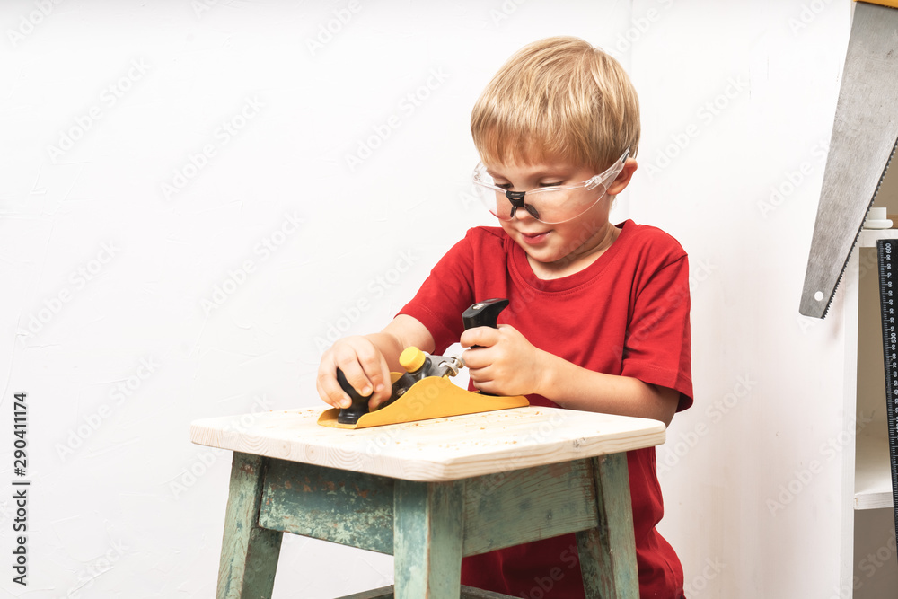 A little boy is planing an old stool with a planer. Training in the skills  of a carpenter and a joiner. Stock Photo | Adobe Stock