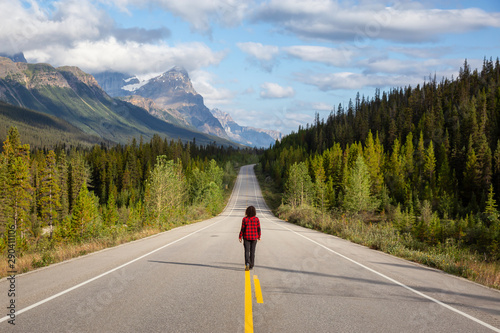 Girl walking down a scenic road in the Canadian Rockies during a vibrant summer morning. Taken in Icefields Parkway, Banff National Park, Alberta, Canada.