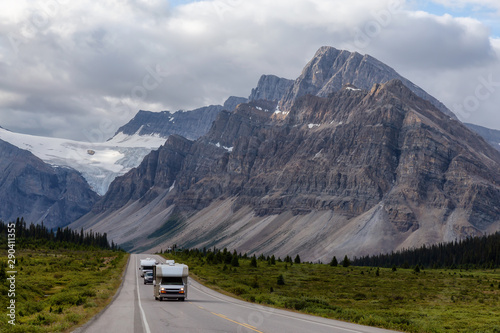 Camper Van driving on a Scenic road in the Canadian Rockies during a vibrant sunny and cloudy summer morning. Taken in Icefields Parkway, Banff National Park, Alberta, Canada.
