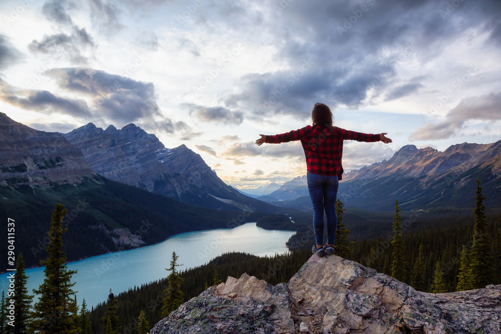 Adventurous girl on the edge of a cliff overlooking the beautiful Canadian Rockies and Peyto Lake during a vibrant summer sunset. Taken in Banff National Park, Alberta, Canada.