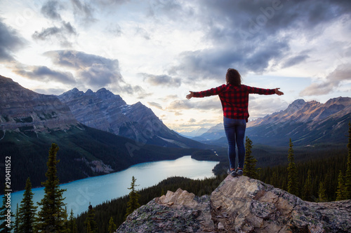 Adventurous girl on the edge of a cliff overlooking the beautiful Canadian Rockies and Peyto Lake during a vibrant summer sunset. Taken in Banff National Park, Alberta, Canada. © edb3_16