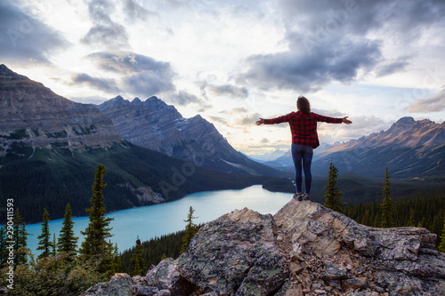 Adventurous girl on the edge of a cliff overlooking the beautiful Canadian Rockies and Peyto Lake during a vibrant summer sunset. Taken in Banff National Park  Alberta  Canada.