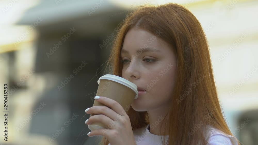 Tired red-haired female drinking coffee outdoors, feeling sleepy, headache Tired red-haired female drinking coffee outdoors, feeling sleepy, headache