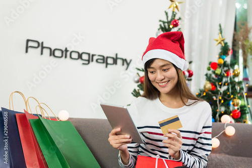 Young asian woman holding credit card and shopping online on a tablet for buy christmas gift at home.