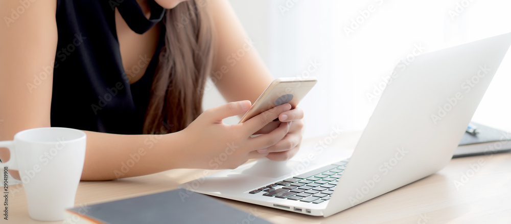 Beautiful young asian woman working laptop computer online to internet and texting message on smart mobile phone, freelance using notebook, business and communication concept.