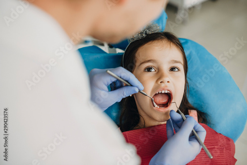 Little cute girl sitting in a stomatology chair with mouth opened during a teeth surgery by a pediatric dentist. photo