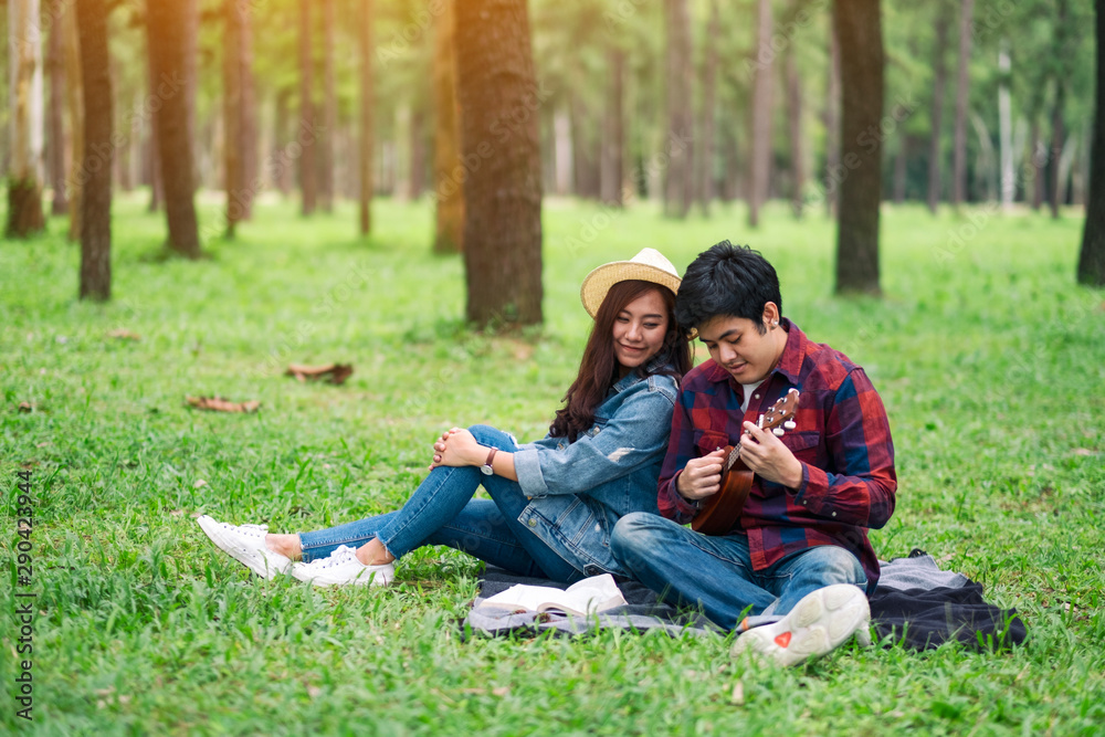 A young couple playing ukulele while sitting together in the woods